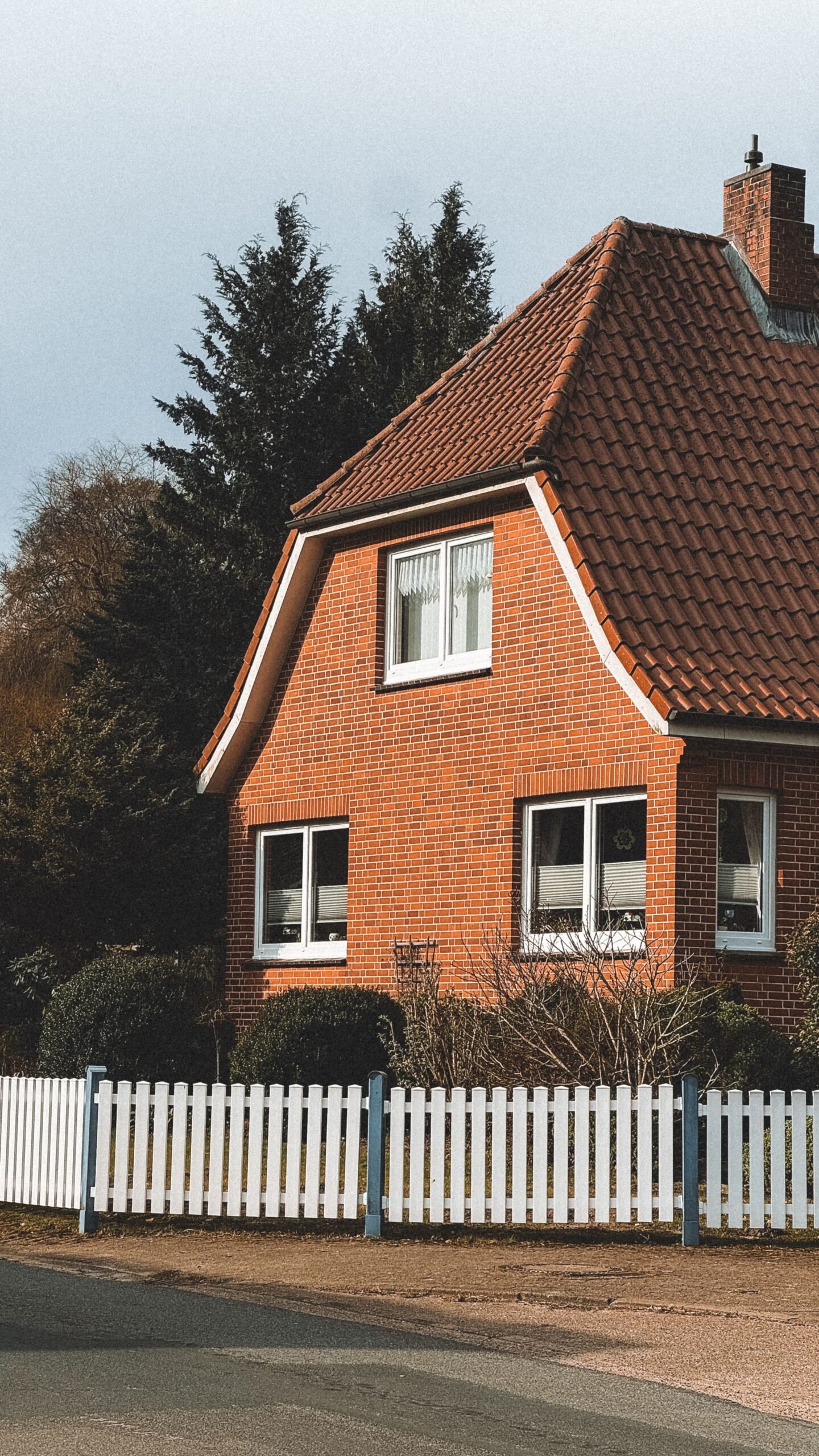 Cozy red brick tiny home with a pitched tile roof behind a white picket fence